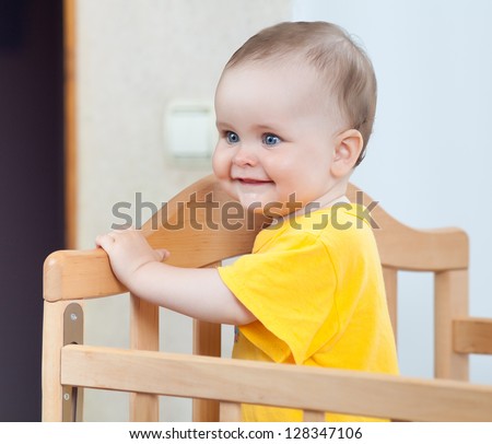 Charming child in the crib. Charming baby in yellow looking away
