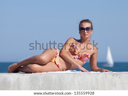 Young woman in bikini at the sea. Attractive woman in swimwear lying on concrete pier looking at camera