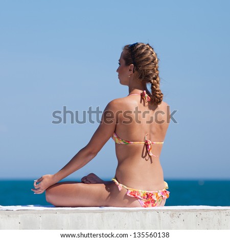Young woman in bikini at the sea. Attractive woman in swimwear doing yoga at the sea. Rear view