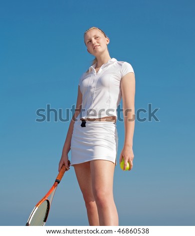 Young blond  tennis-player with tennis racket and tennis balls in white sportwear is standing on seashore