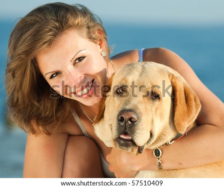 Young woman with Labrador male dog on the background of the sea. Girl embracing her dog and looking at camera