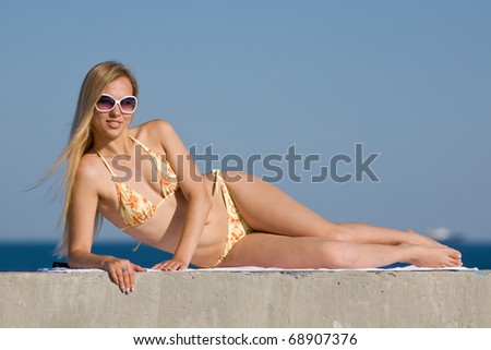 Blonde in bikini and sunglasses at the sea. Attractive young woman in bikini lies on the beach