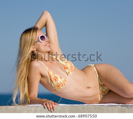 Blonde in bikini and sunglasses at the sea. Attractive young woman in bikini lying on the beach