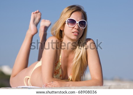 Blonde in bikini and sunglasses at the sea. Attractive young woman in bikini lies on the beach
