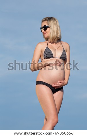 Pregnant woman in swimwear outdoors. Attractive expectant mother in bikini on background of the sea