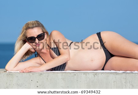Pregnant woman in swimwear outdoors. Attractive expectant mother in bikini lies and looks  through sunglasses at camera
