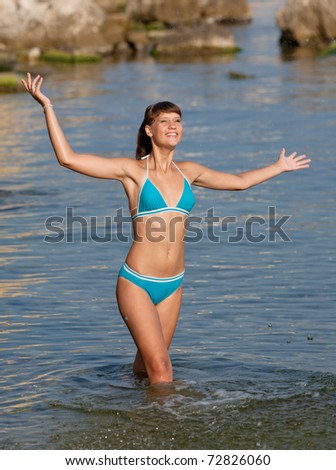 Attractive girl is standing knee-deep in water. Young woman in blue swimwear is splashing at the sea