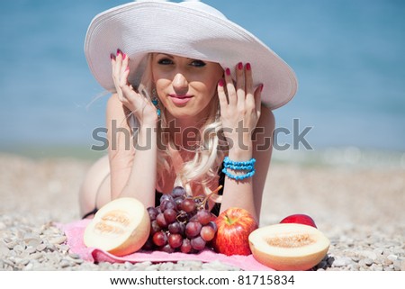 Attractive blonde at the sea. Girl in swimwear and hat lying on the beach behind the fruit