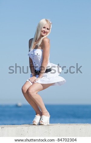 Blonde holds her skirt blown by wind. Girl laughing on open air