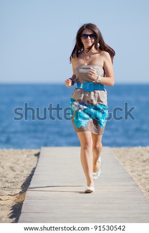 Attractive young woman on the beach. Attractive young woman in dress and sunglasses running along the beach