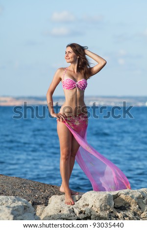 Girl at the sea. Attractive young woman is posing on background of sea. Lady in pink swimwear with arm raised on the beach