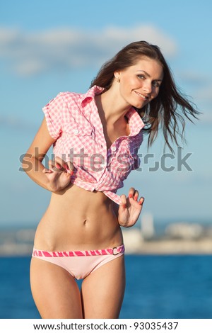 Girl at the sea. Attractive young woman is posing on background of sea. Lady in pink shirt on the beach