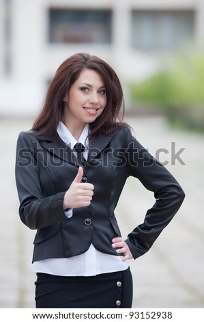 Attractive business woman on background of building. Cute business woman showing thumb up smiling