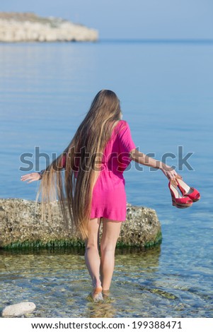 Long-haired girl on the beach. Young woman in red comes into water