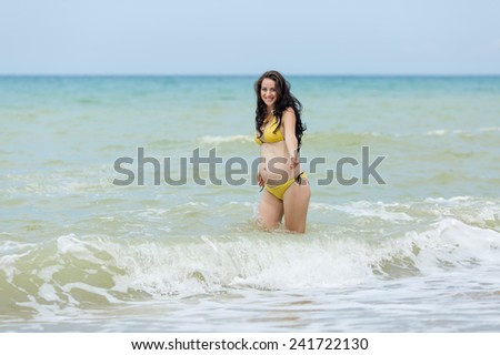 Expectant mother playing in the sea. Pregnant woman in yellow bikini on the beach
