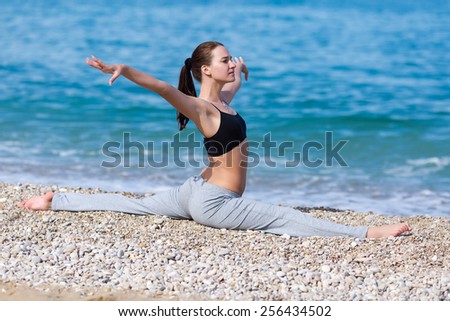 Sportswoman doing gymnastic twine on pebble beach. Female fitness on seashore