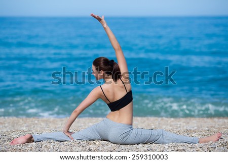 Sportswoman doing gymnastic twine on pebble beach. Female fitness on seashore
