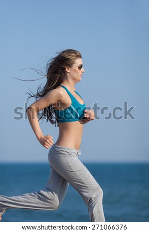 Jogging. Slim girl in sport bra and sunglasses runs along the seashore