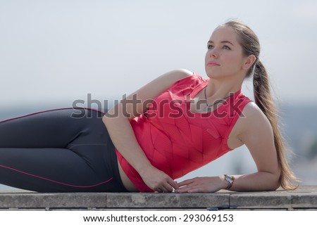 Girl with ponytail poses outdoors. Young woman in sportswear lying on side looking up