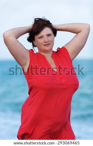 Woman in red at the sea. Overweight young woman in red blouse posing with arms raised against the sea