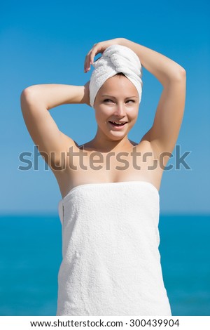 Girl at the sea. Funny young woman wrapped in a towel with turban, made from other towel, on head. She posing against the sea, looking away