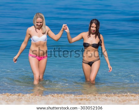 Girls at the sea. Two young women in swimwear walking hand in hand in water