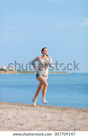 Jogging. Woman in jeans shorts and grey sport uniform runs along seashore
