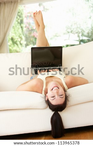 Woman Lying Upside Down On Sofa Using Laptop