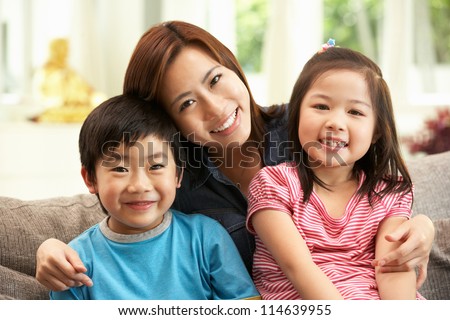 Chinese Mother And Children Sitting On Sofa At Home Together