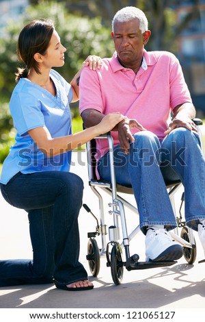 Carer Pushing Unhappy Senior Man In Wheelchair