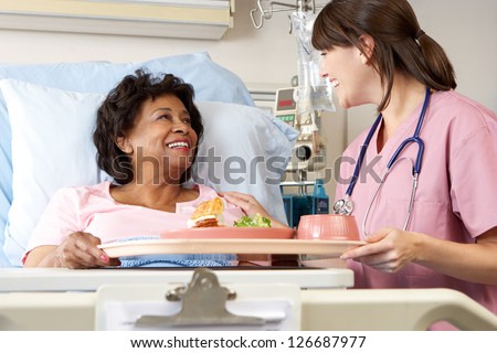 Nurse Serving Senior Female Patient Meal In Hospital Bed