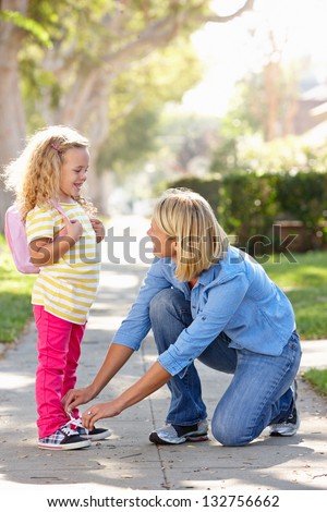 Mother Helping Daughter Tie Shoe Laces On Walk To School