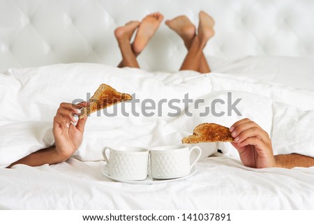 Couple Hiding Under Duvet Enjoying Breakfast In Bed