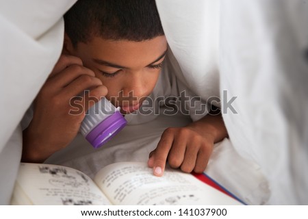Boy Reading Book With Torch Under Duvet
