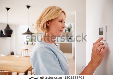 Close Up Of Mature Woman Adjusting Central Heating Temperature At Home On Thermostat 商業照片 © 