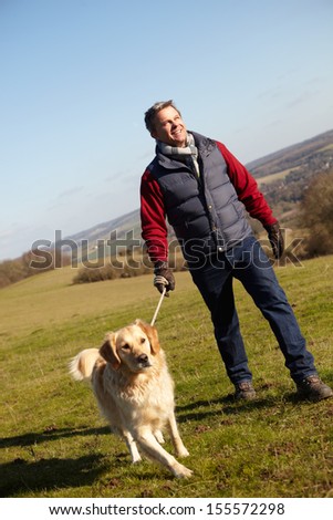 Man Taking Dog On Walk In Autumn Countryside