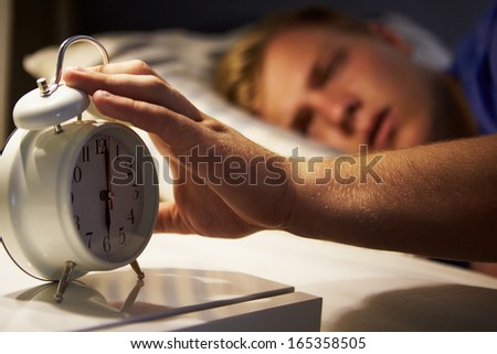 Teenage Boy Waking Up In Bed And Turning Off Alarm Clock
