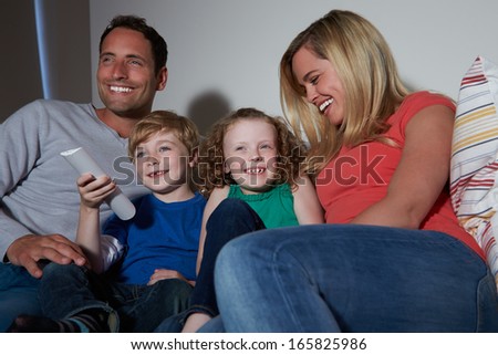 Family Sitting On Sofa Watching TV Together