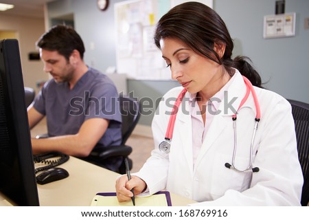 Female Doctor With Male Nurse Working At Nurses Station