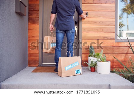 Rear View Of Home Delivery Driver Outside Front Door With Takeaway Food Bags Ringing Doorbell