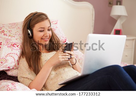 Teenage Girl Lying On Bed Using Laptop Whilst Texting