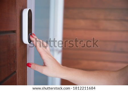 Close Up Of Woman Ringing Front Doorbell Equipped With Security Video Camera