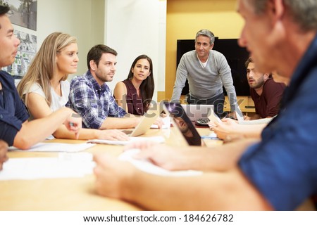 Male Boss Addressing Meeting Around Boardroom Table