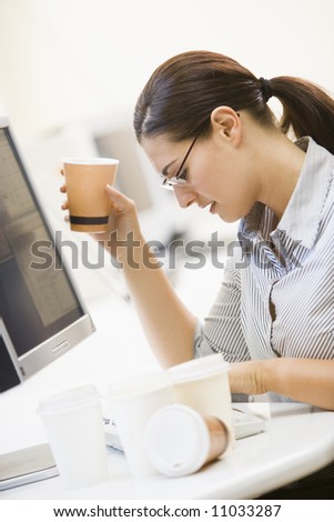 Female Office Worker At Desk Drinking Coffee