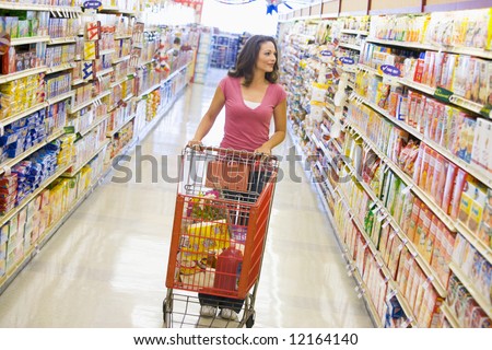 Woman pushing trolley along supermarket grocery aisle