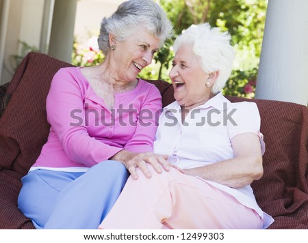 Senior female friends chatting together sitting on garden seat