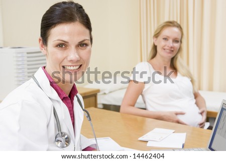 Doctor with laptop and pregnant woman in doctor\'s office smiling