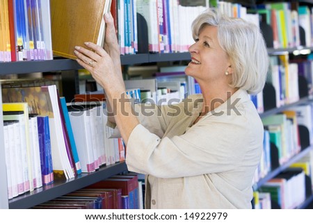 Senior woman pulling a library book off shelf