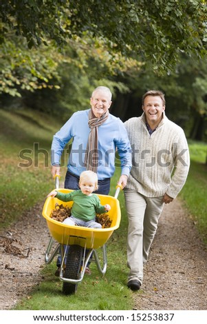 Grandfather with grandson and son pushing wheelbarrow along autumn path