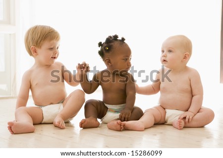 Three babies sitting indoors holding hands